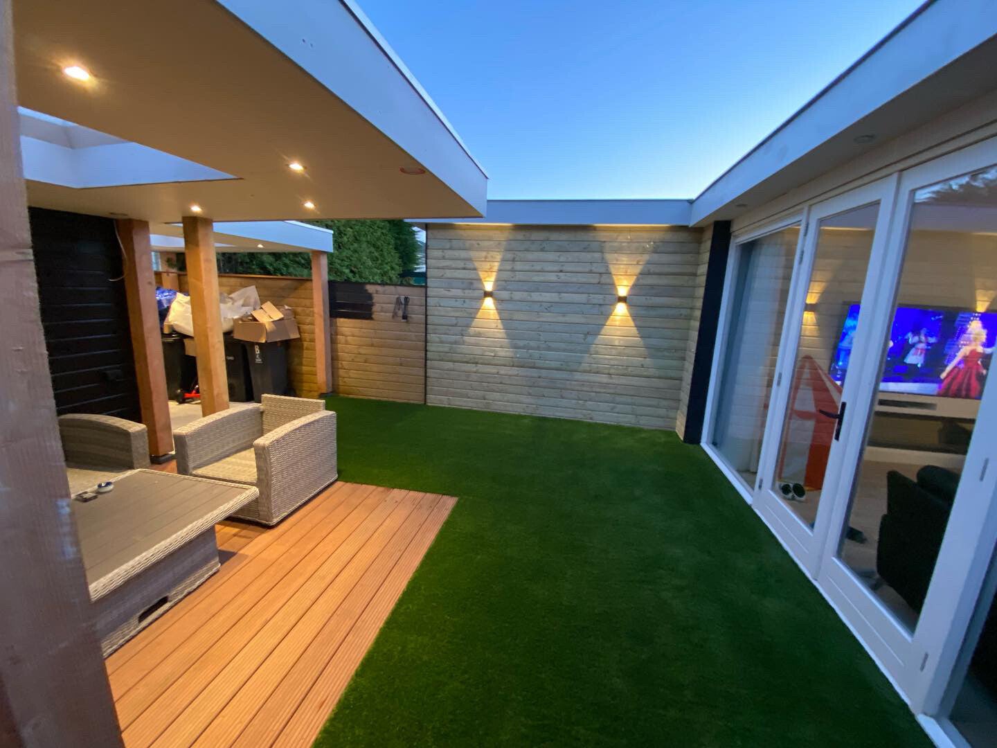 Overdekt terras en tuin in de avond met wandverlichting